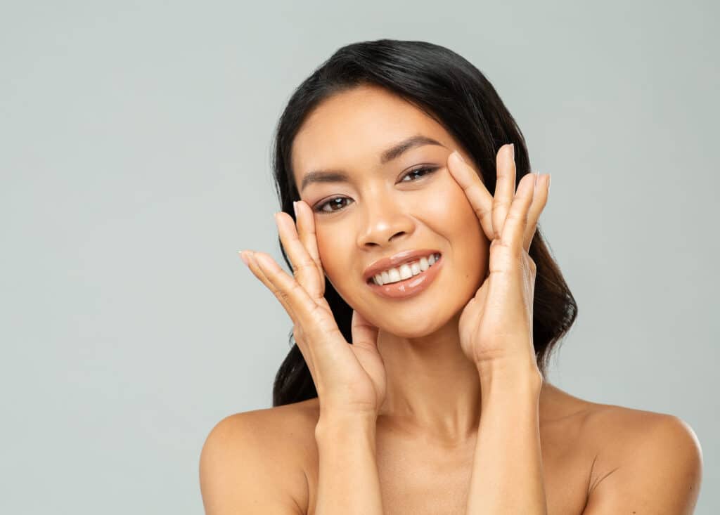 Happy Asian Woman with Hands on Eyes over isolated white background. Women Face Skin Care Treatment. Laser Vision Surgery Correction. Dermal Fillers cosmetics and facial hydration