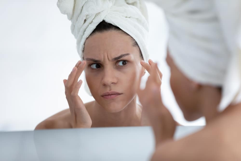 Woman examining forehead lines while comparing BOTOX, Dysport, and DAXXIFY treatment options.
