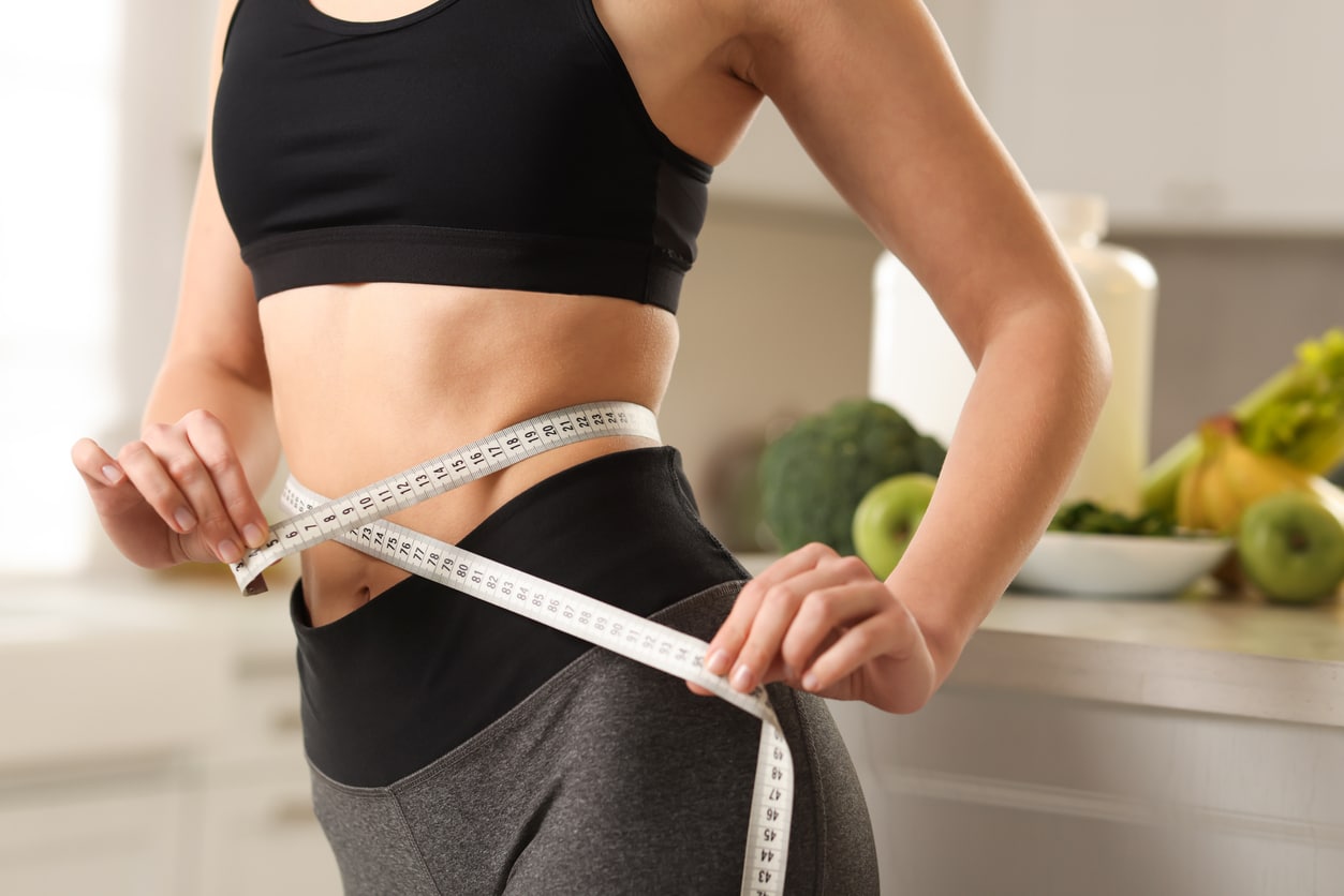 Woman measuring her waist with a tape measure, representing weight management and hormone-related weight loss challenges.